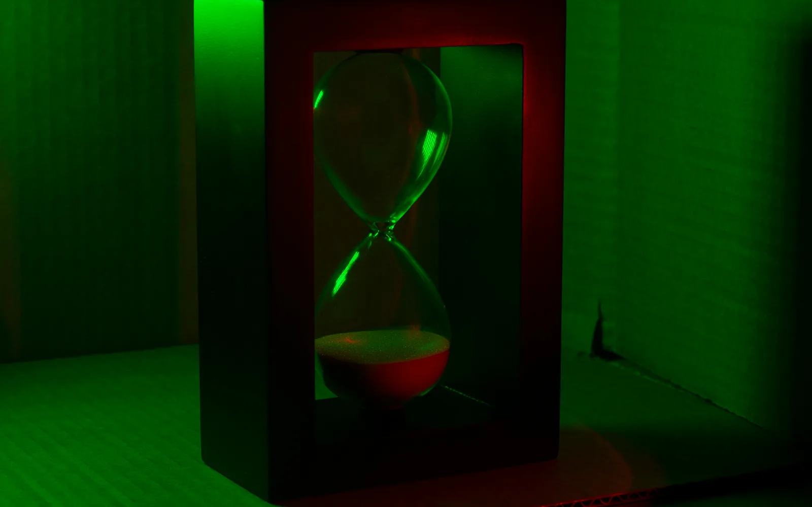 An hourglass sits in a frame under green light.