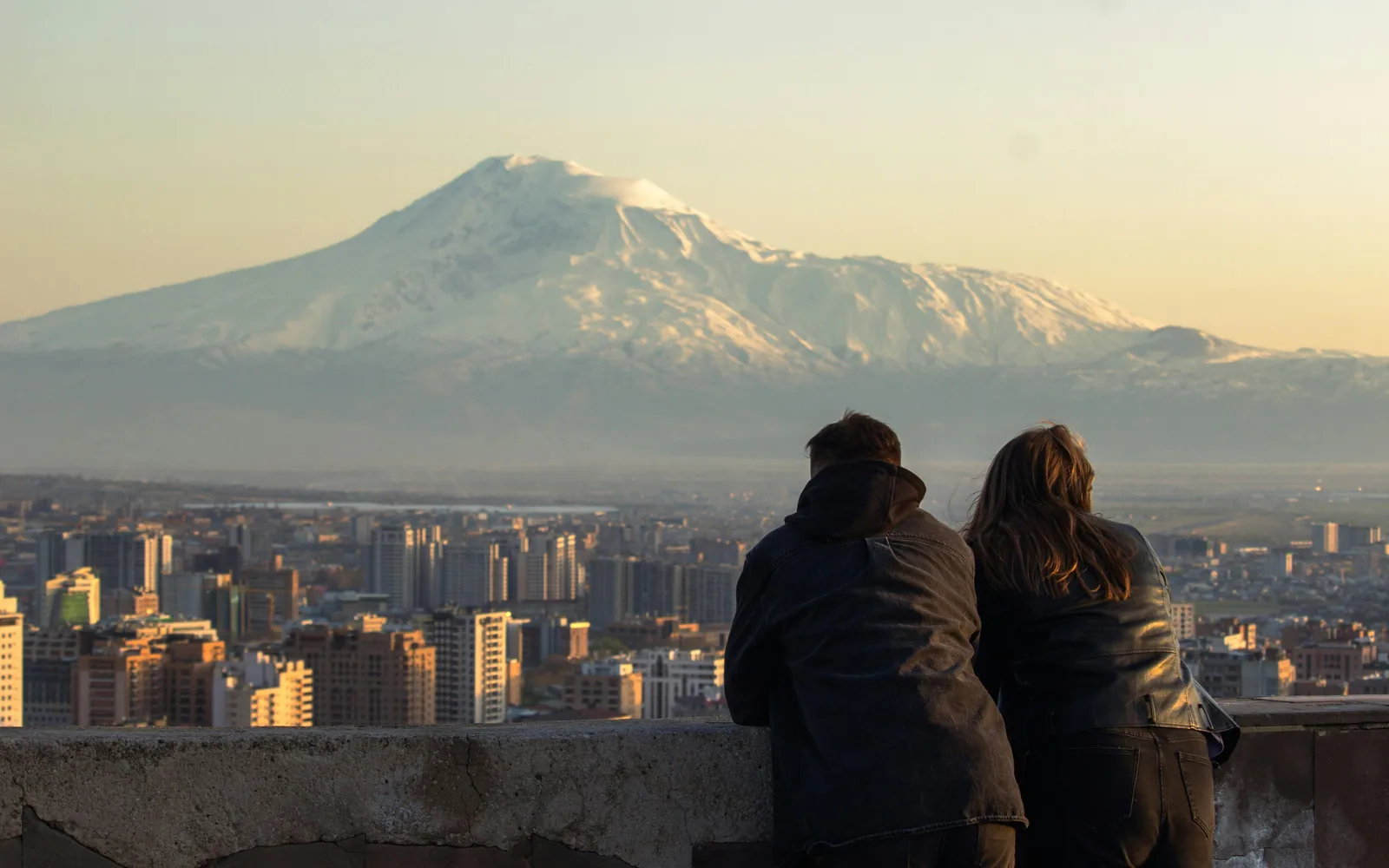 Couple looking at a snow-capped mountain over cityscape.