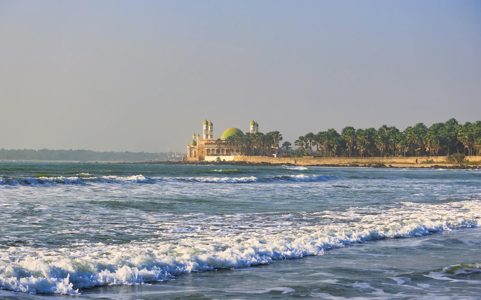 Waves crash on a beach near a domed building.