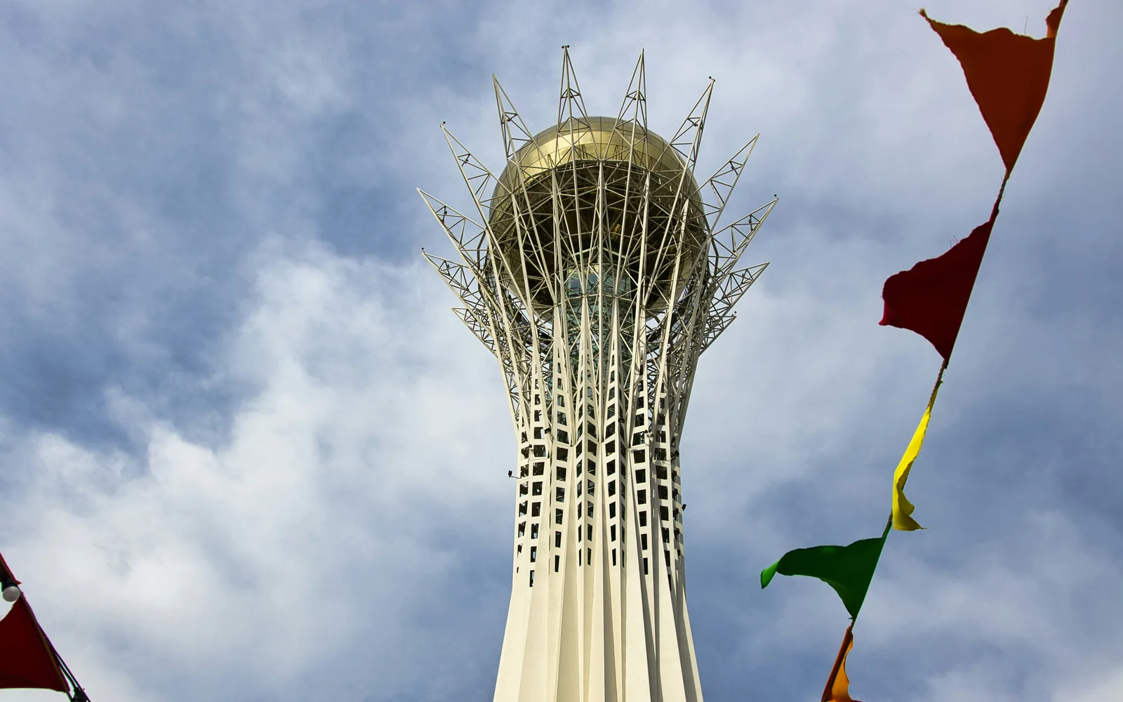 Bayterek tower with colorful flags against cloudy sky