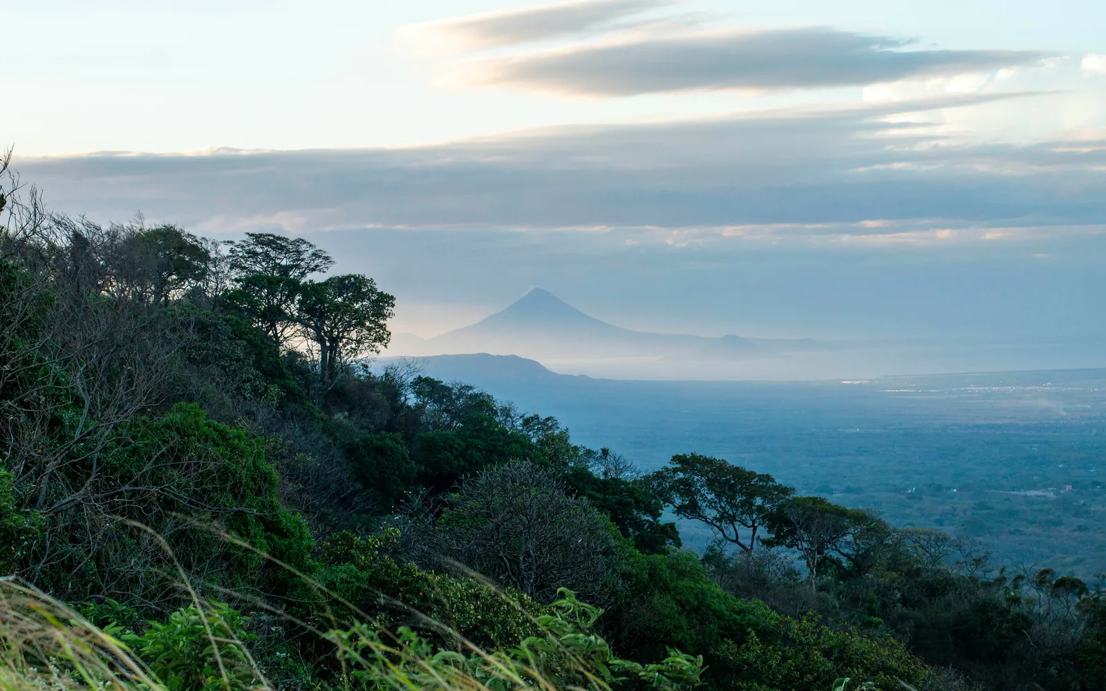 From Mirador Zaira Julissa López, layered peaks guard Lake Managua under pastel skies, green valleys evoke nature's grand, serene fusion.