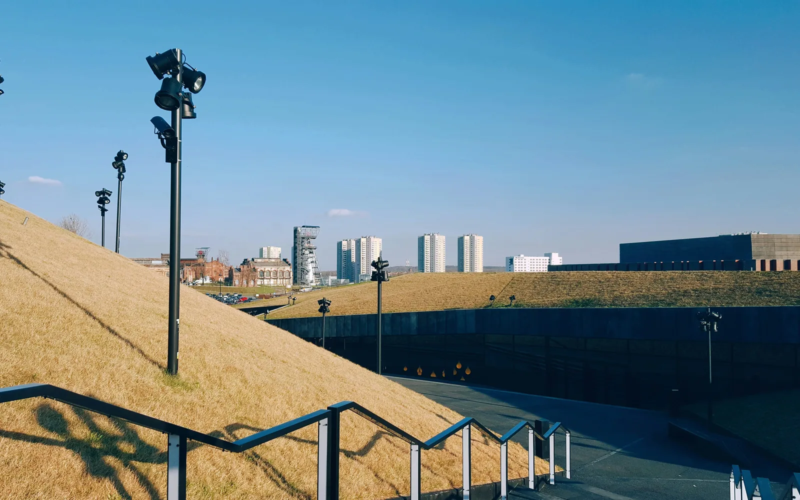 A sunny day with a grassy hill and city buildings.