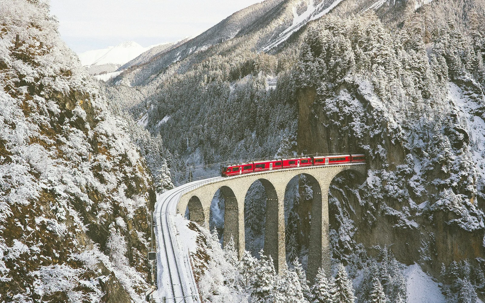 Red Swiss train approaching across an alpine mountain landscape