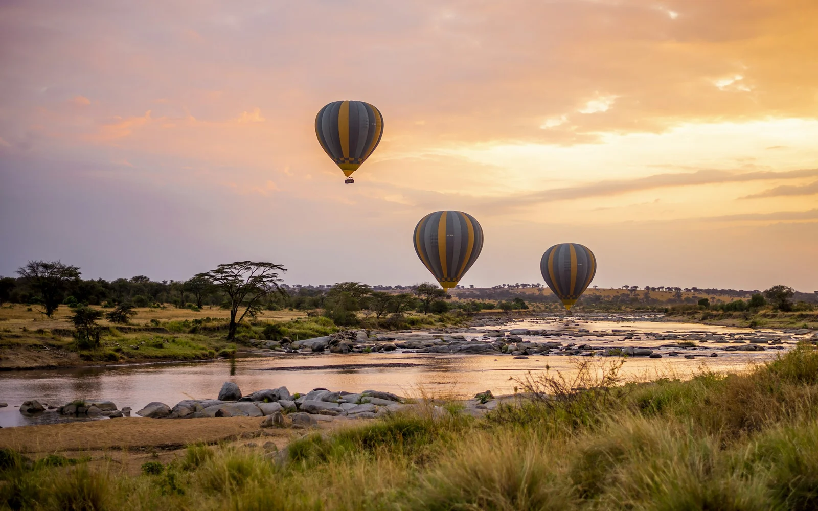 Three hot air balloons flying over a river in the Serengeti, Tanzania