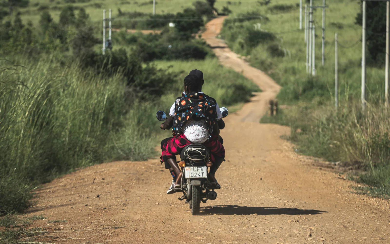 Woman with a baby strapped to her back rides on the back of a motorbike